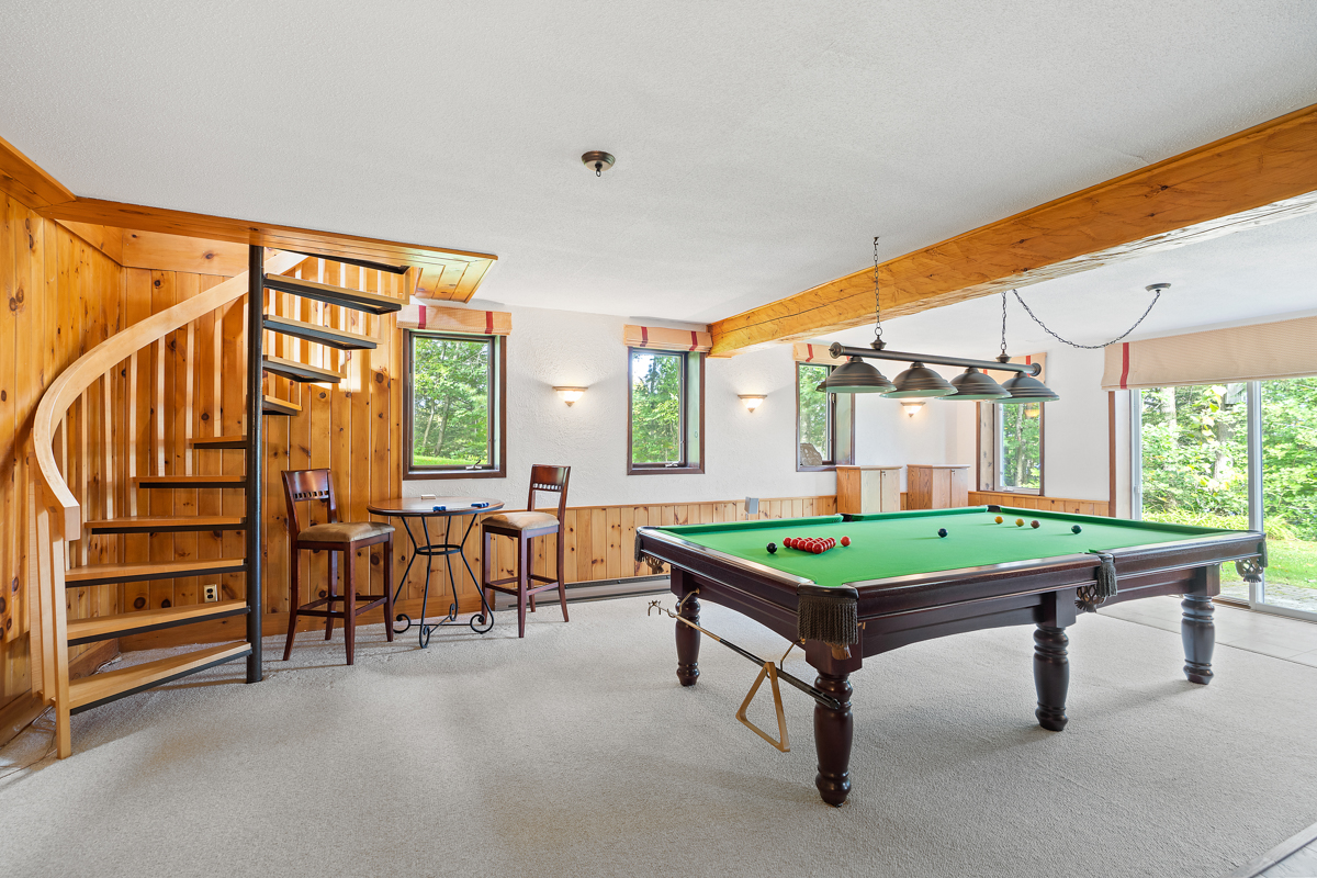 A lower-level rec room with a pool table and carpeted floors.
