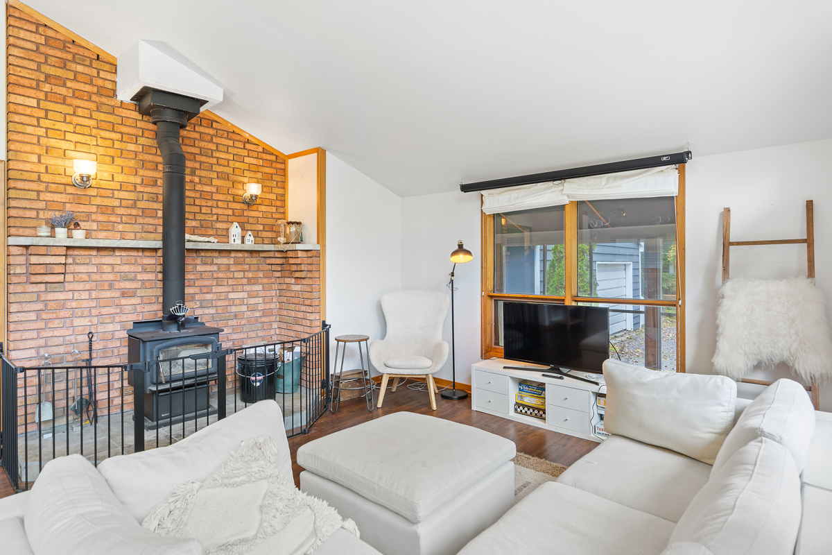 A bright living area with a white couch, a television, and a wood-burning fireplace.