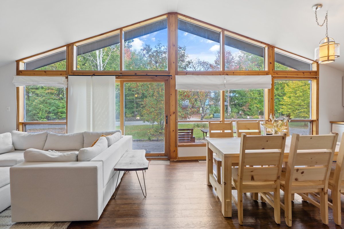 Floor-to-ceiling windows span the front wall of a cottage bungalow. A door leads to the front porch..