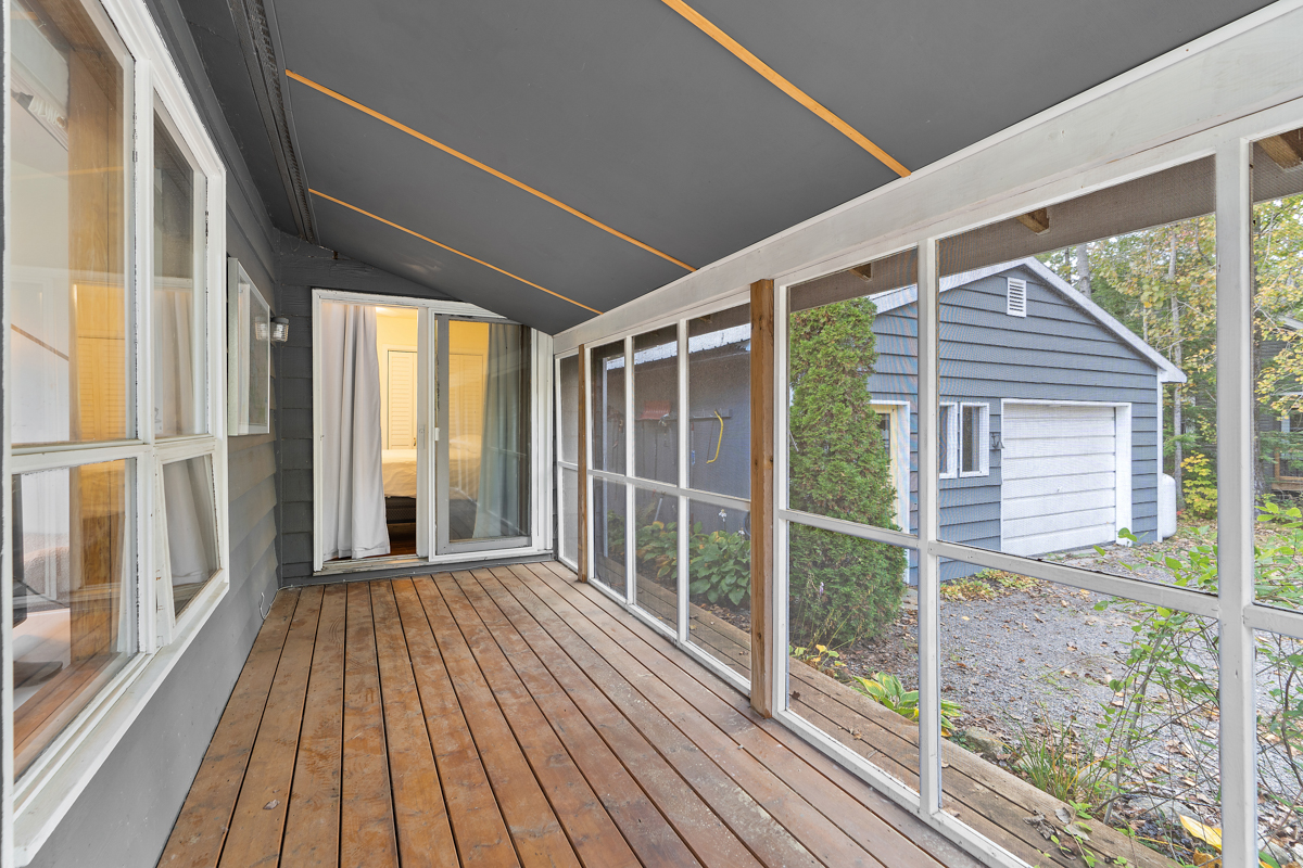 A screened-in porch on the side of a cottage, with a door that leads to one of the bedrooms inside.