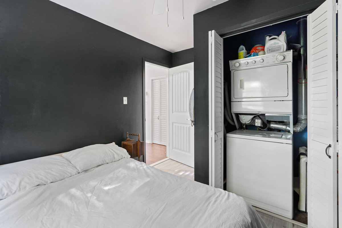 A small bedroom with black walls, a bed, and a washing machine and dryer stacked in a closet.