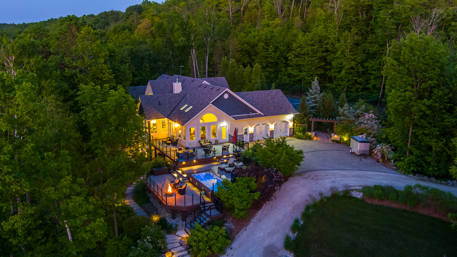 A large luxury property with a big outdoor patio, lit up with lots of lights and surrounded by green trees.