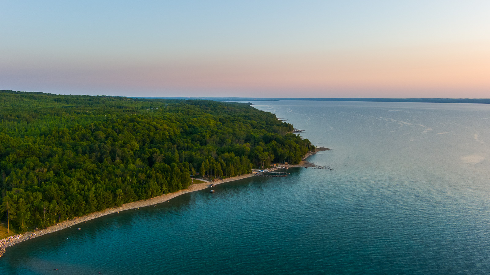 A calm lake and land with lots of green trees.