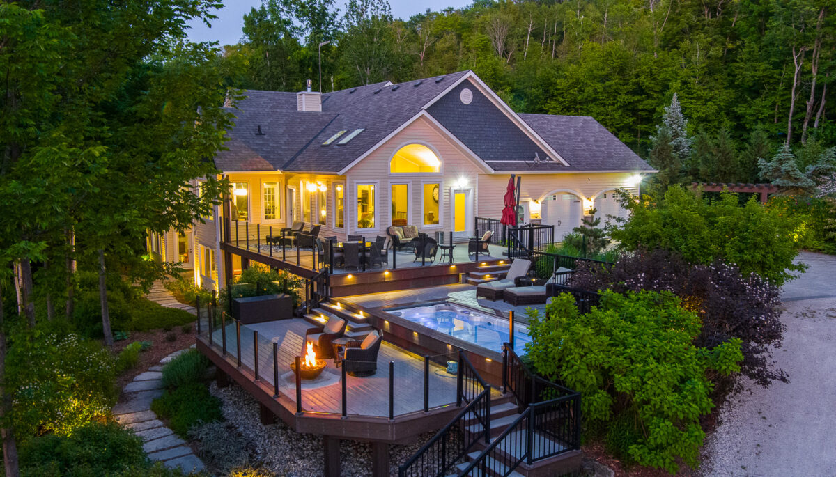 A large luxury property with a big outdoor patio, lit up with lots of lights and surrounded by green trees.