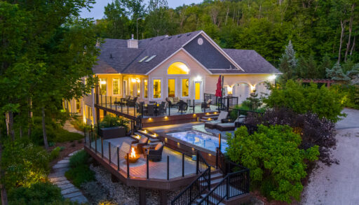 A large luxury property with a big outdoor patio, lit up with lots of lights and surrounded by green trees.