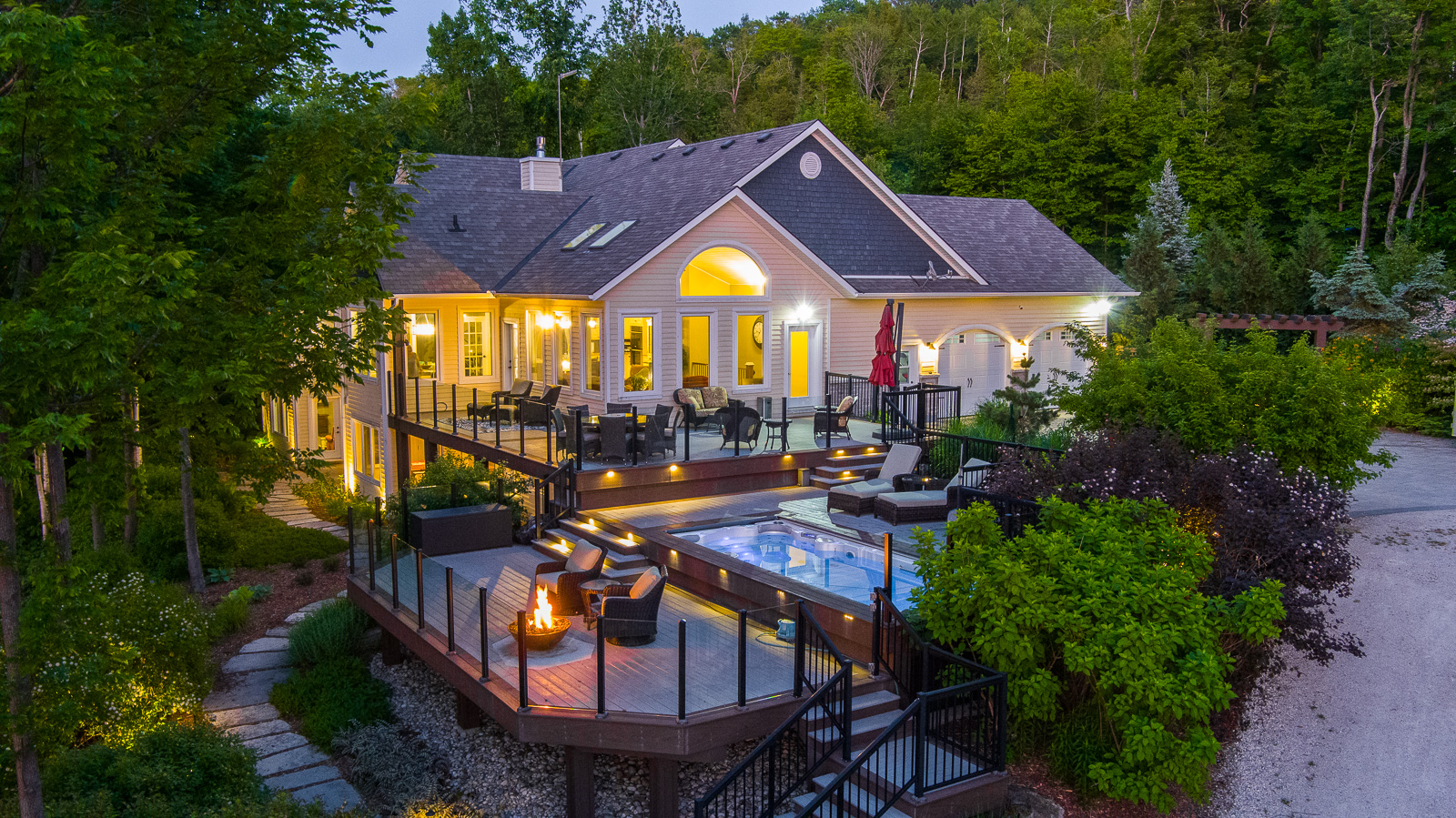 A large luxury property with a big outdoor patio, lit up with lots of lights and surrounded by green trees.