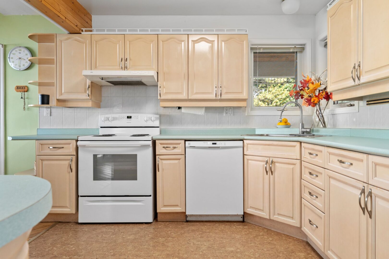 A kitchen with light green countertops, beige cabinets, and white appliances.