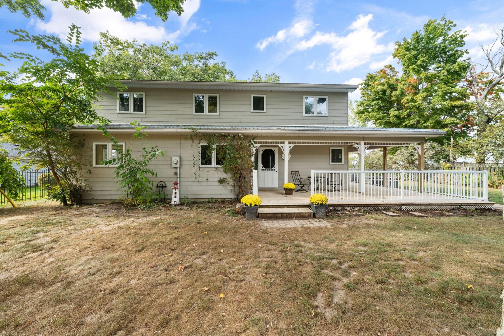 A two-story cottage on a grassy lot, with a large wrap-around porch and a white fence.