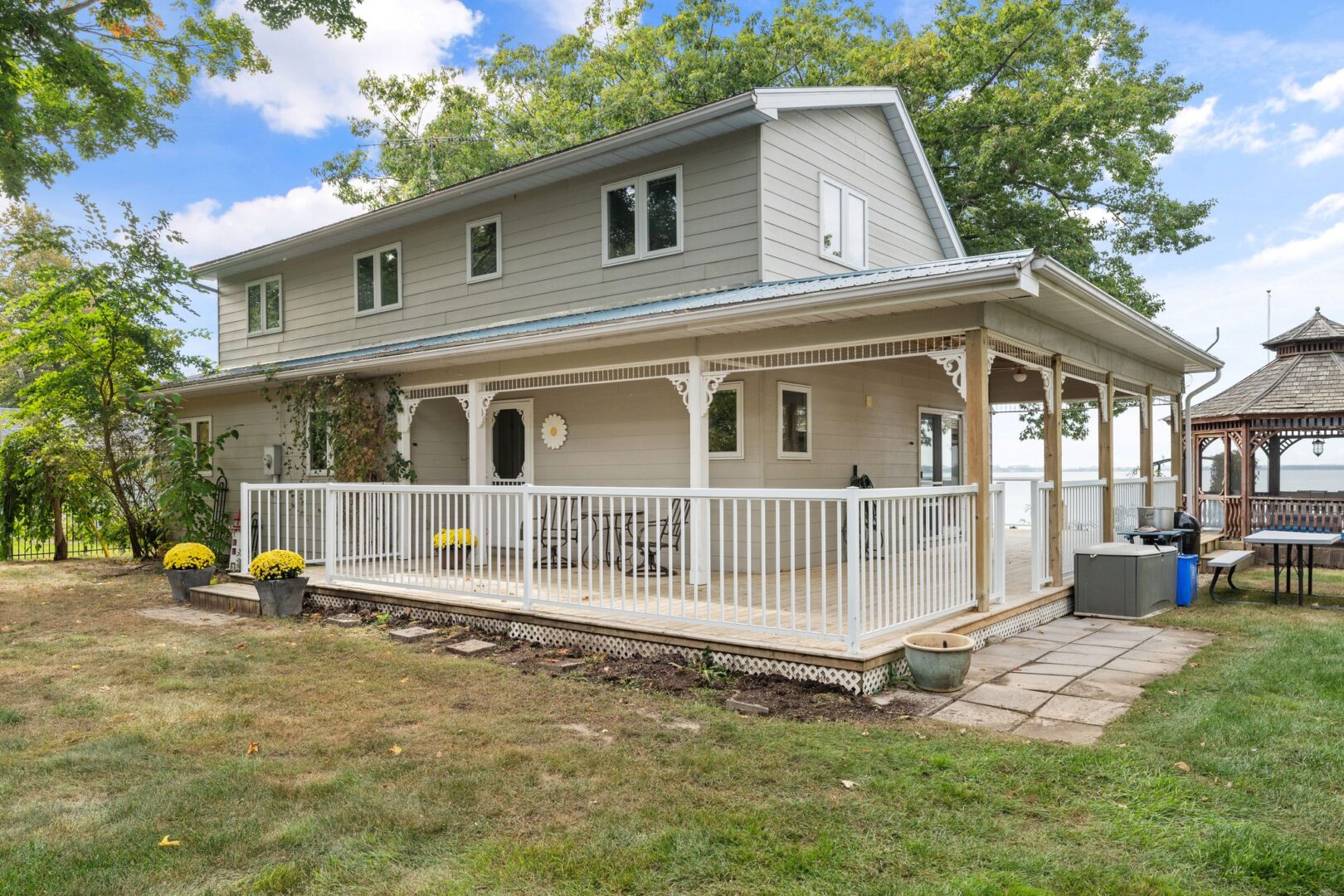 A two-story cottage on a grassy lot, with a large wrap-around porch and a white fence.