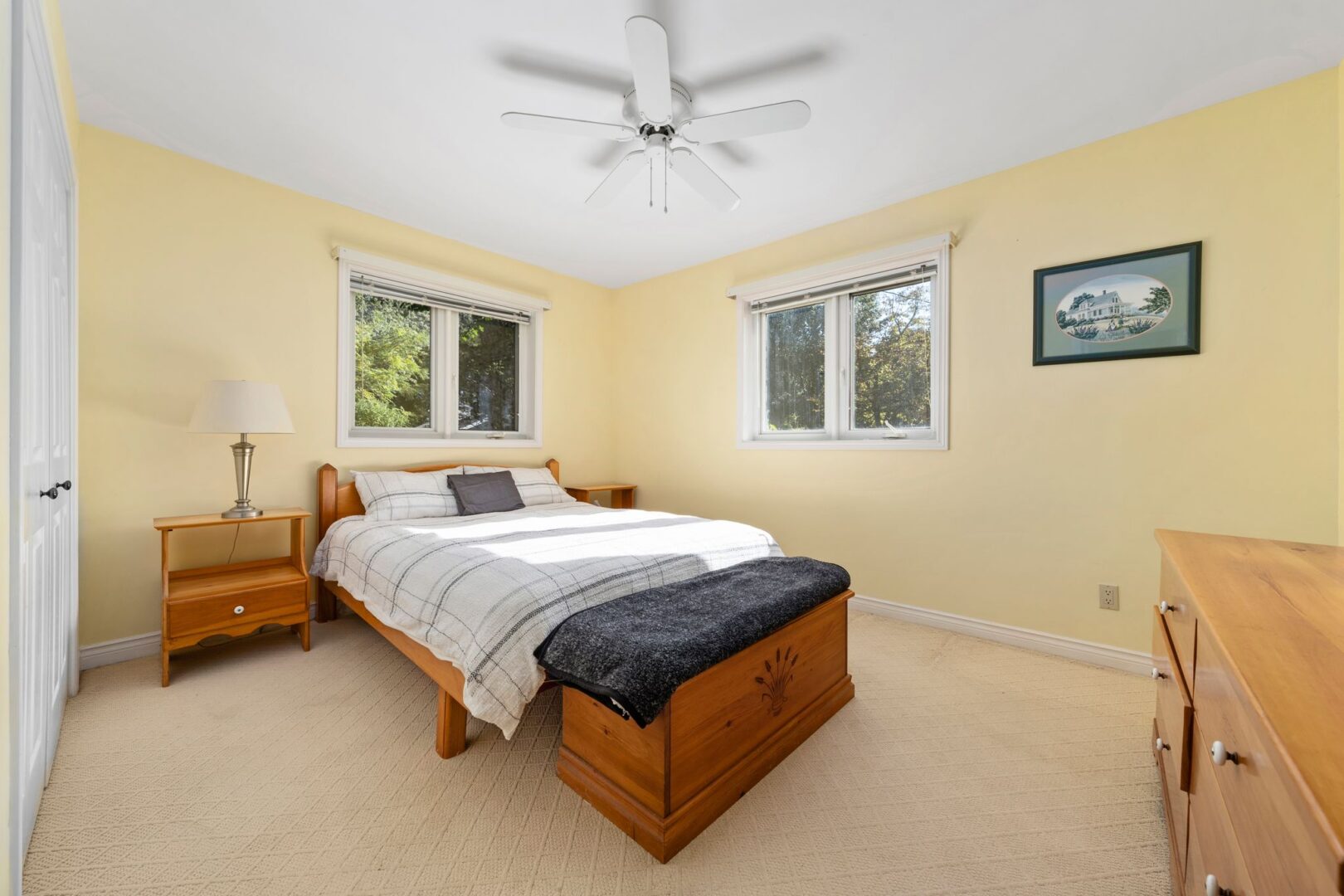 A bright bedroom with light yellow walls, a ceiling fan, and a big bed.