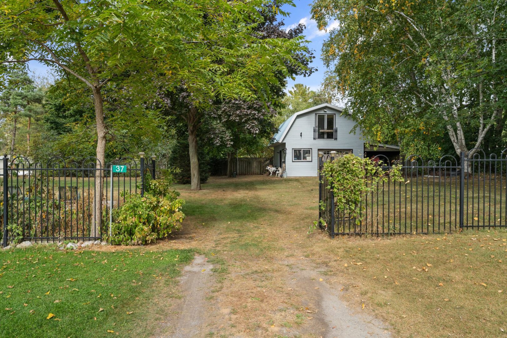 A driveway leads through an open gate of a fence into a grassy cottage property.