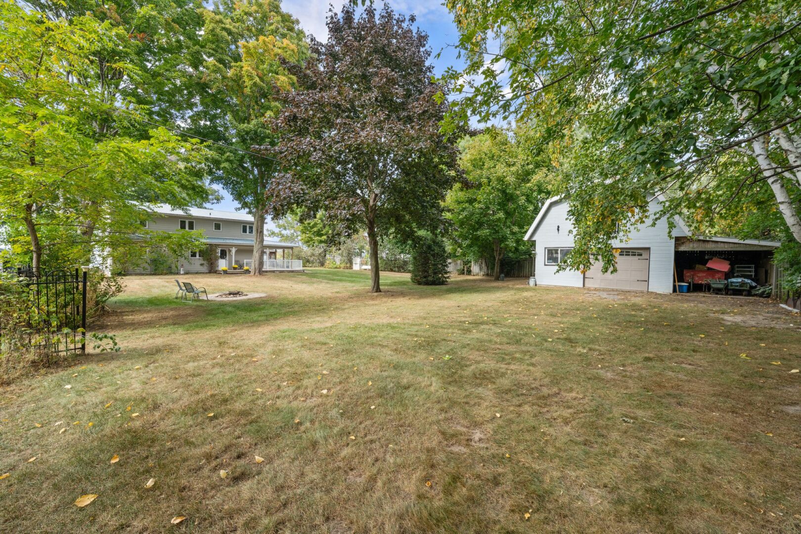 A large, grassy lot with a two-story cottage, a detached garage, and a small fire pit.