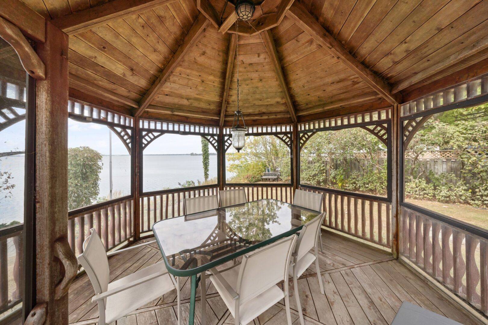 Inside a large outdoor gazebo with a dining table and chairs, with a view of the lake.