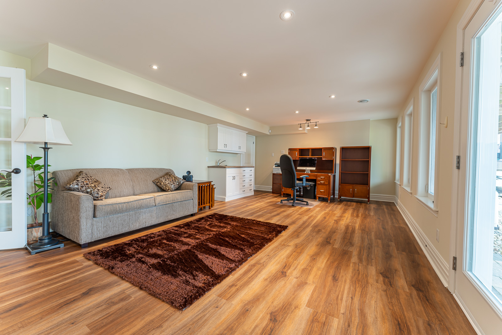 A wide lower-level living space with a couch, a desk, and a small sink area.