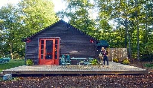 a woman sweeps leaves off of her cottage deck