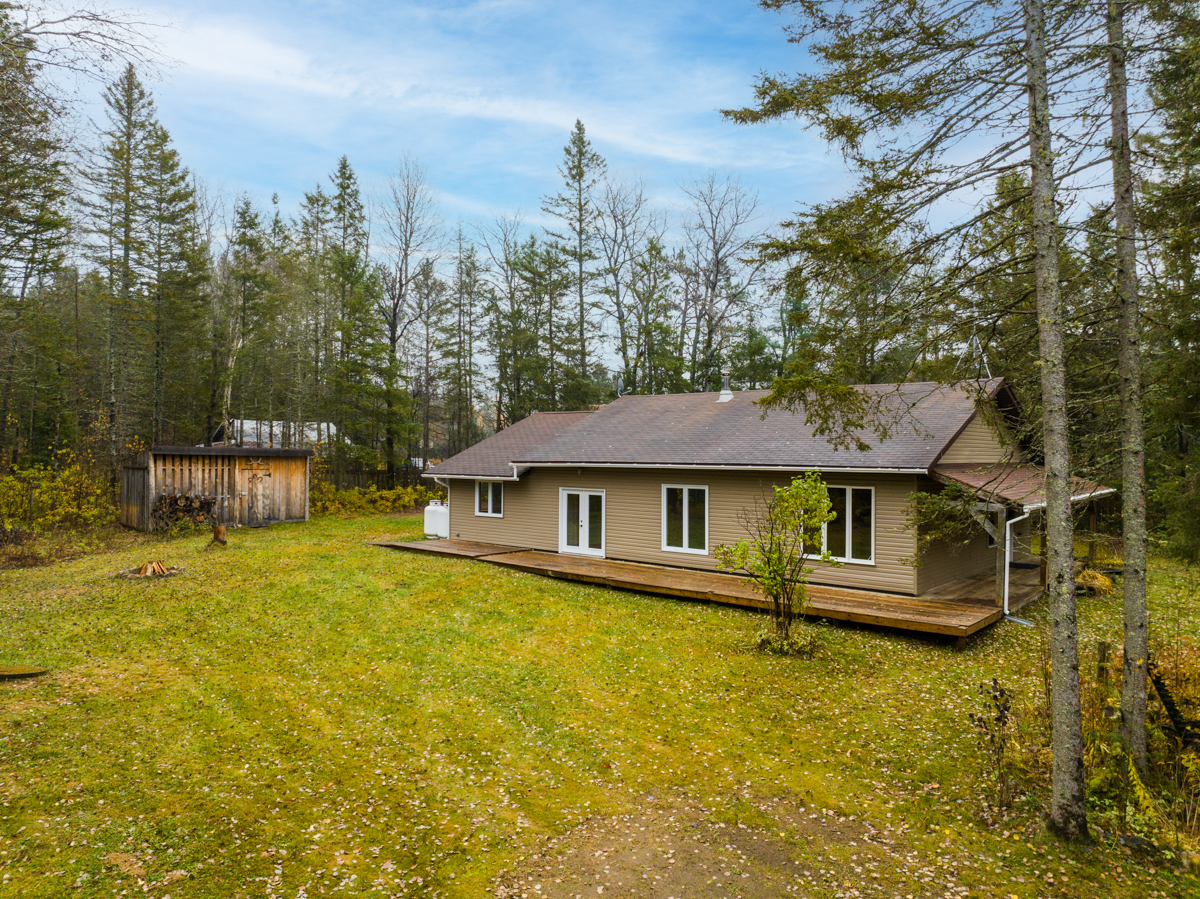 A bungalow-style home in a wide grassy area surrounded by forest.