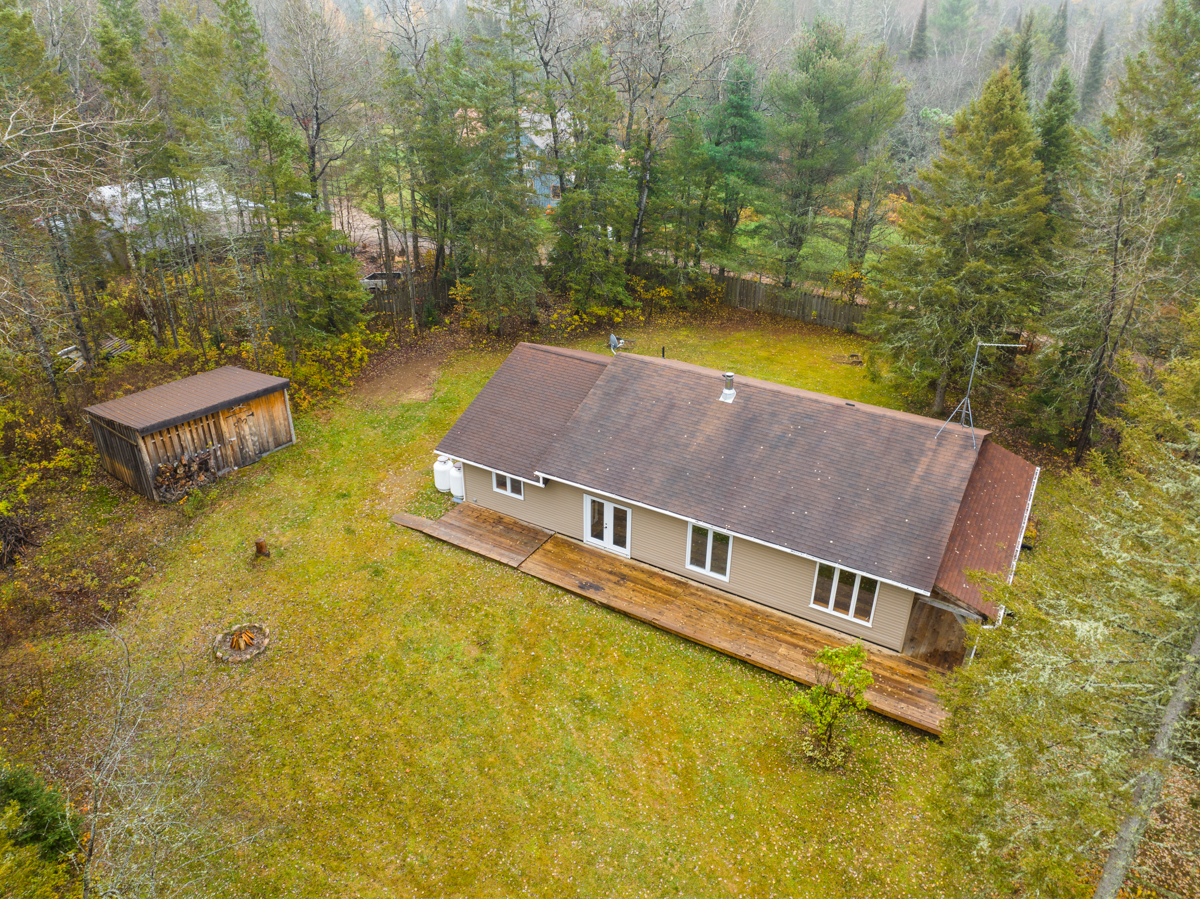 Overhead view of a bungalow-style home in a wide grassy area surrounded by forest.
