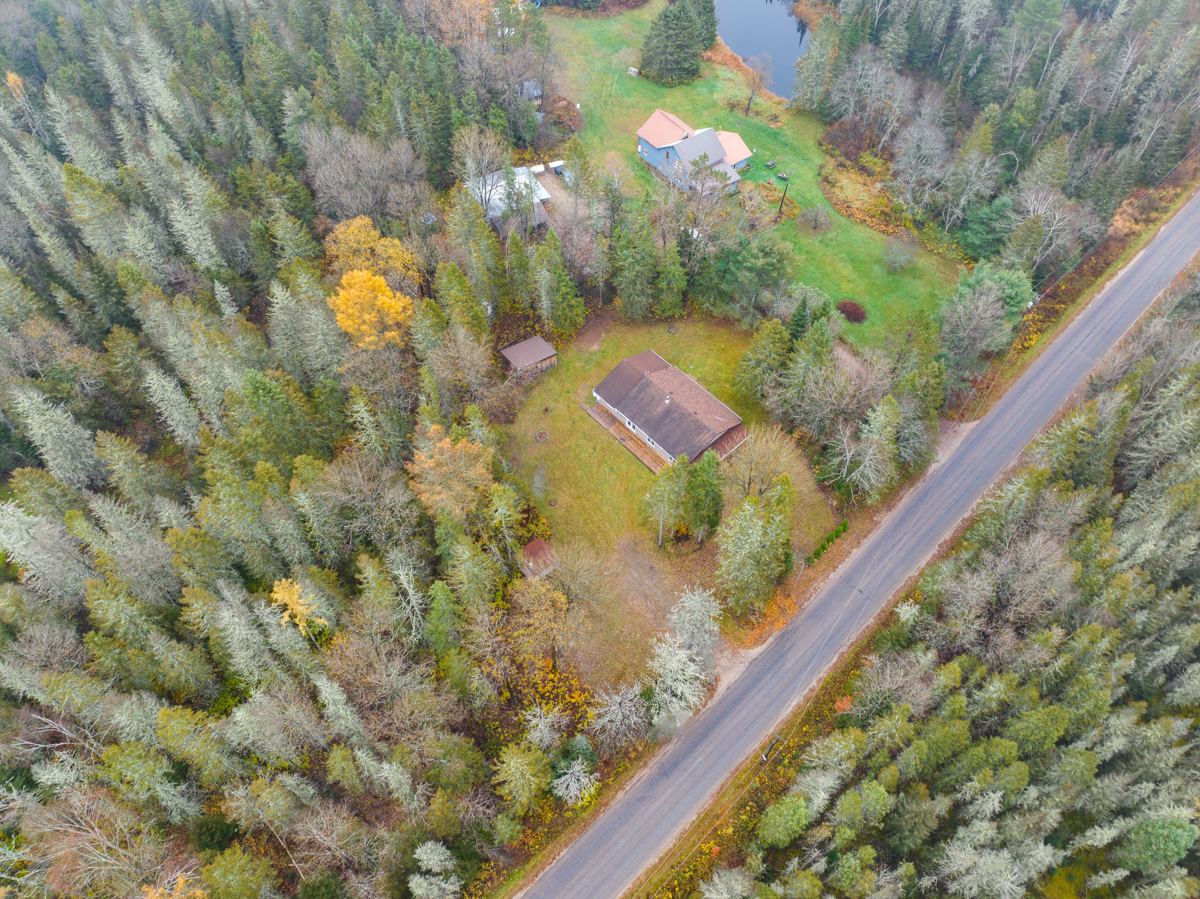 Overhead view of a cottage-country home surrounded by forest and next to a long road.