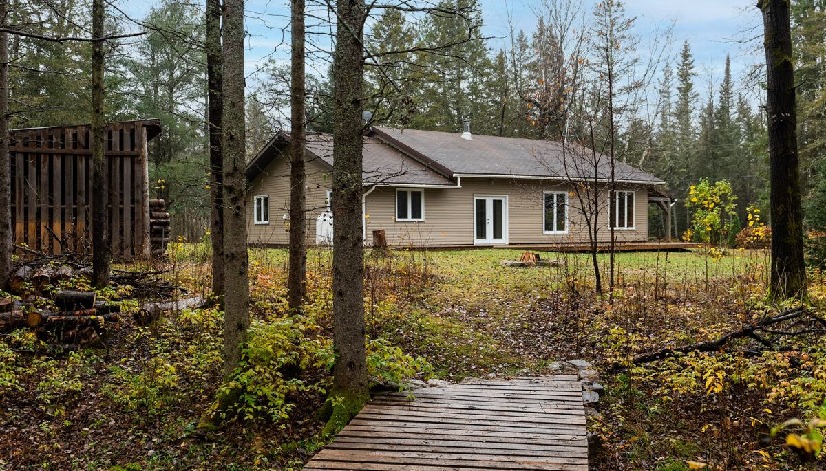 A wooden walkway leads from a residential property into a forested area.