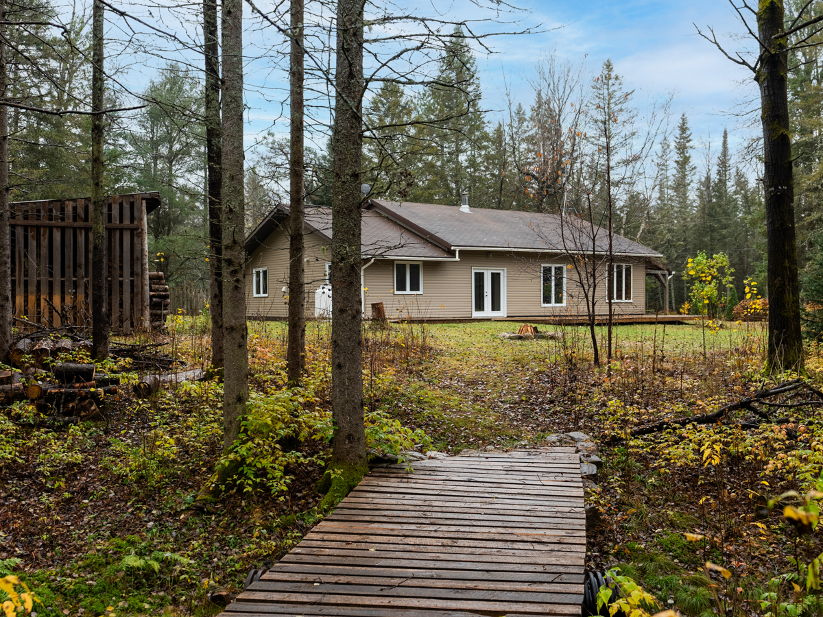 A wooden walkway leads from a residential property into a forested area.