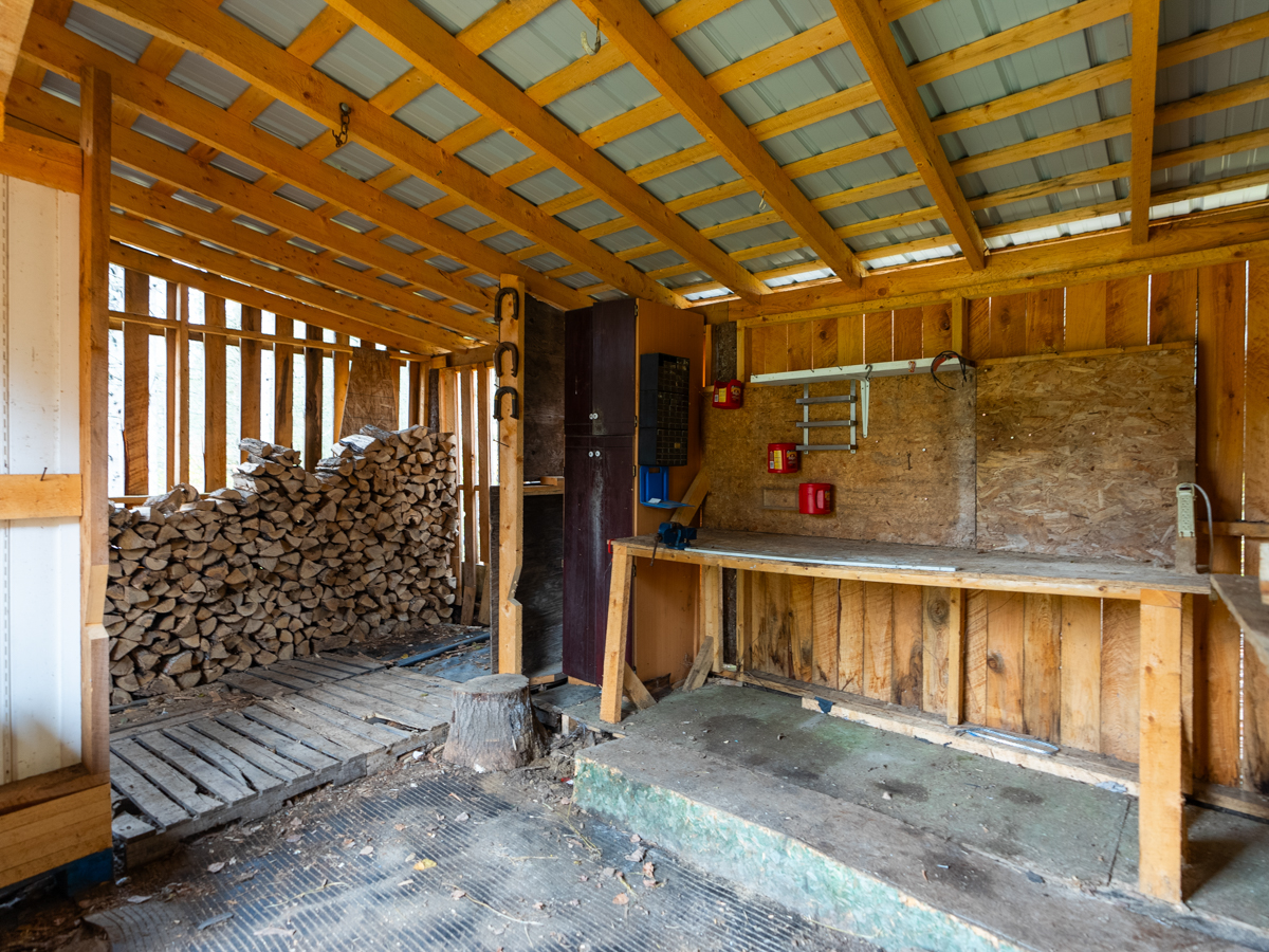 Inside a big walk-in wood shed, with a stack of fire logs and a work table.