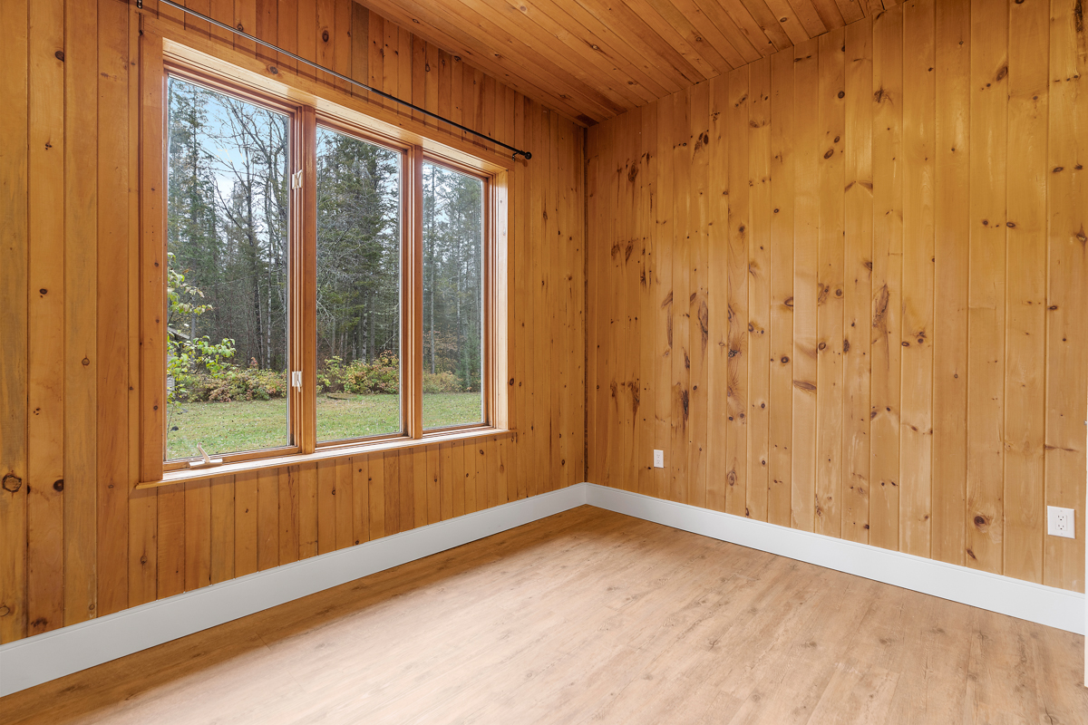 A big, empty bedroom with a large window and wood panelling on the walls and ceiling.
