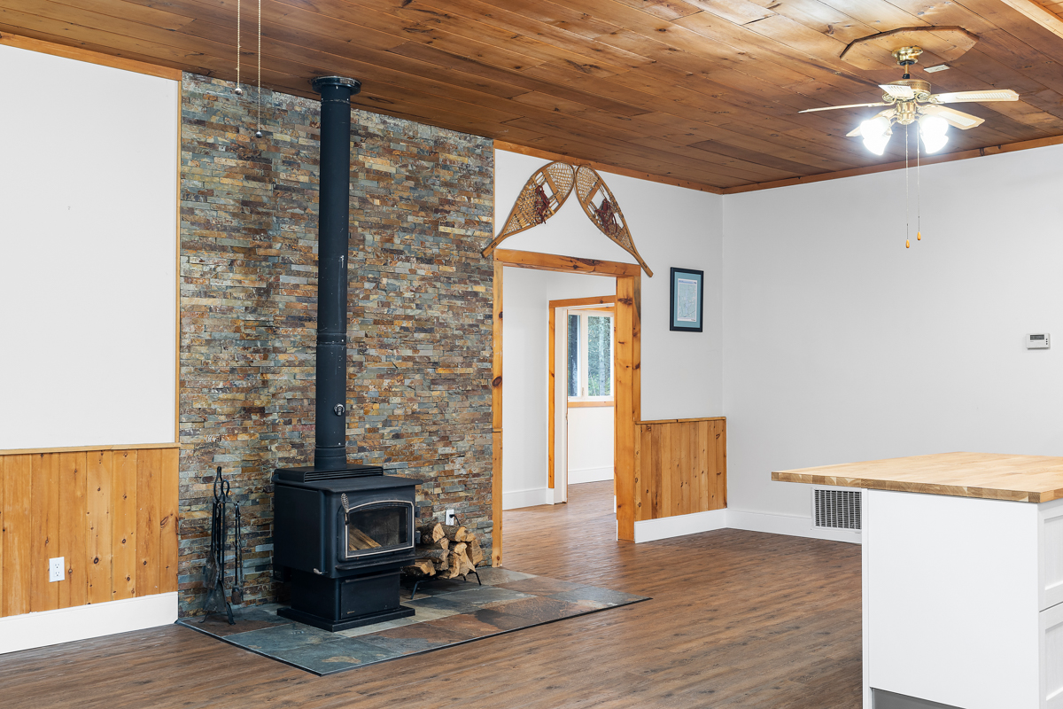 A wood stove sits on a tiled area, in front of a floor-to-ceiling section of stone wall.