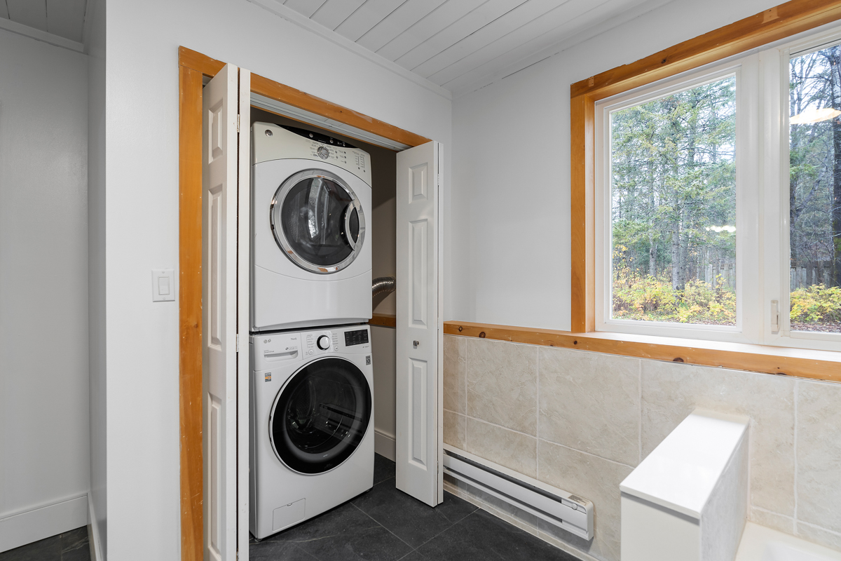 A stacked washing machine and dryer sit in a closet in a big bathroom.