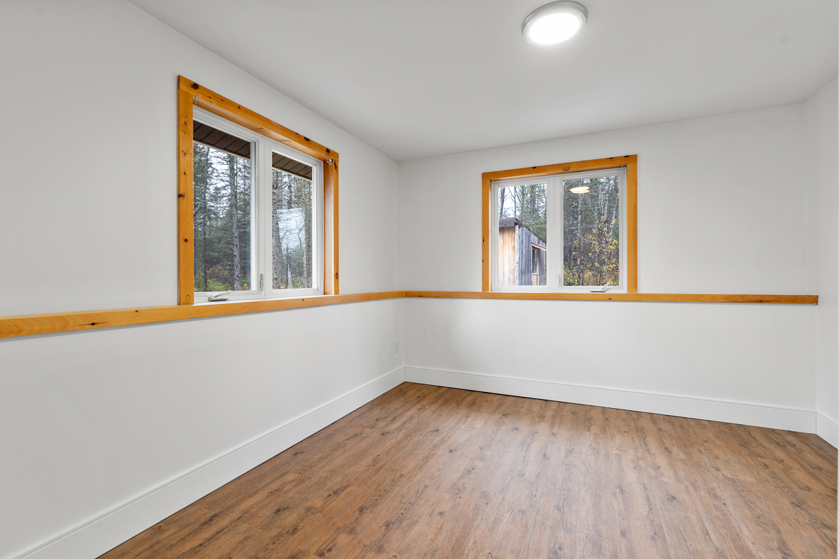 A large, empty bedroom with white painted walls and two windows..