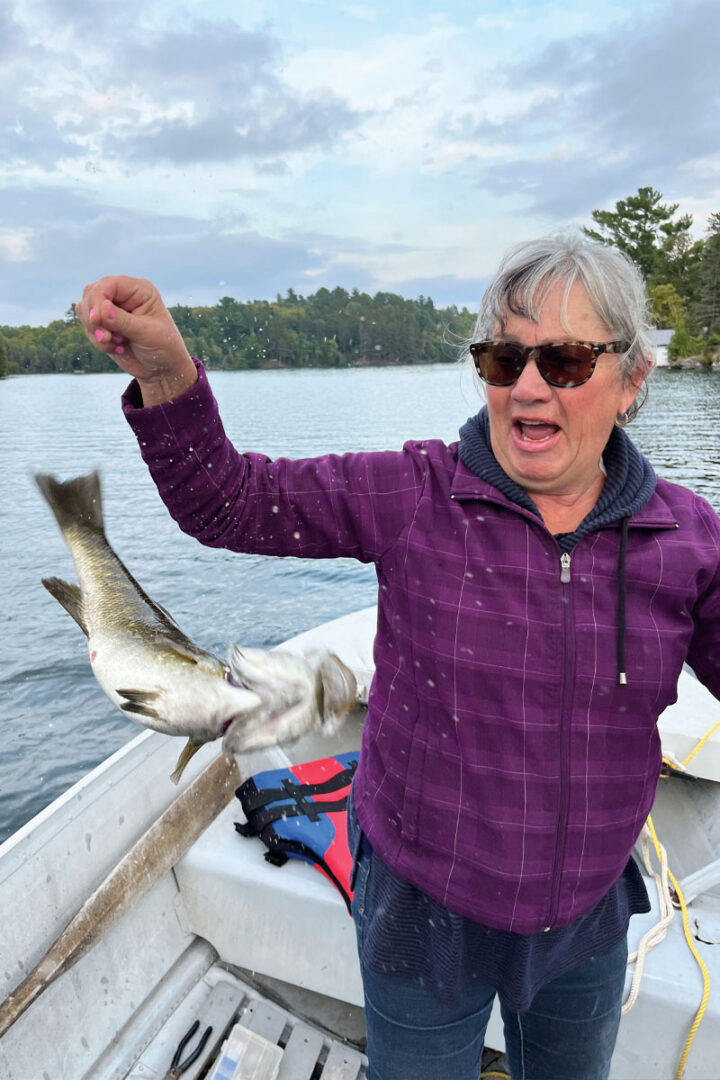 A woman fishing on a boat with a large fish flapping around on the line, her face aghast.