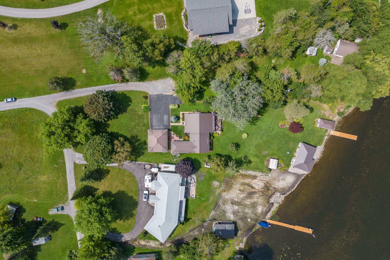 Aerial view of a waterfront bunkie with lots of private green space, neighboured by two other large properties. A dock extends into the water at the shoreline.