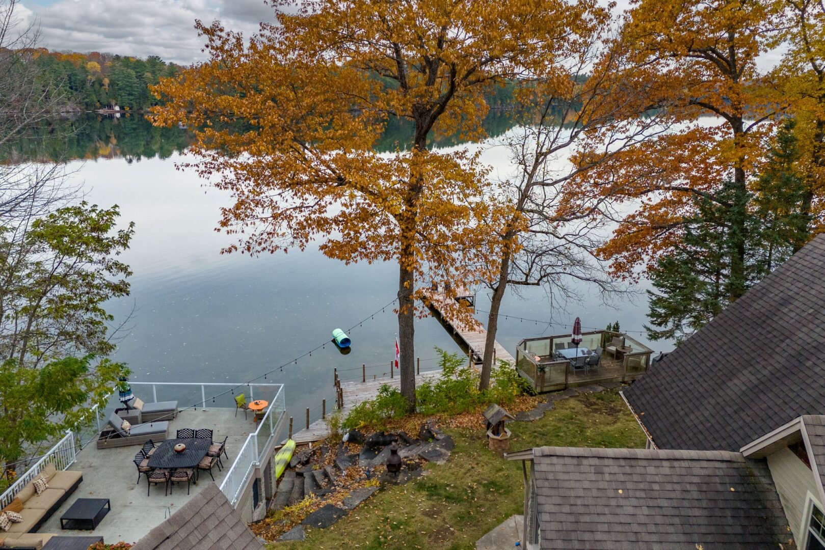Looking out over a large cottage property toward the lake. The property has two decks with outdoor furniture, a grassy area, and a large dock extending into the lake.