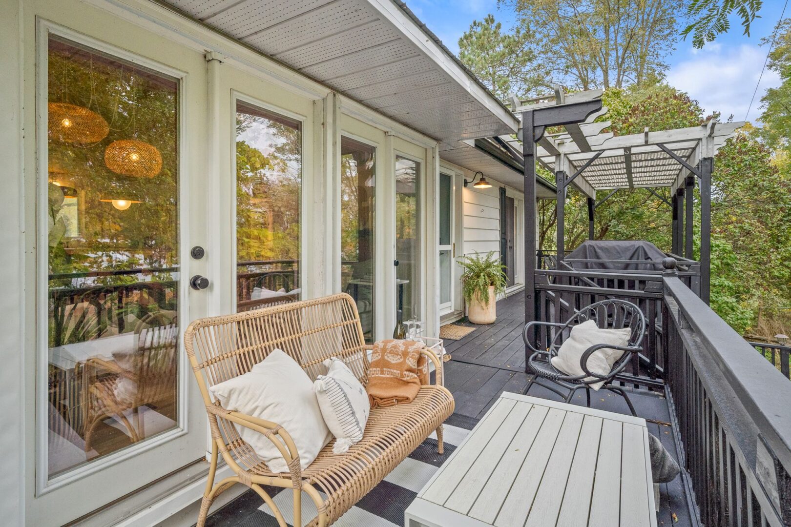 Two basket chairs sit on the front porch of a raised bungalow, in front of double glass doors that lead into the house.