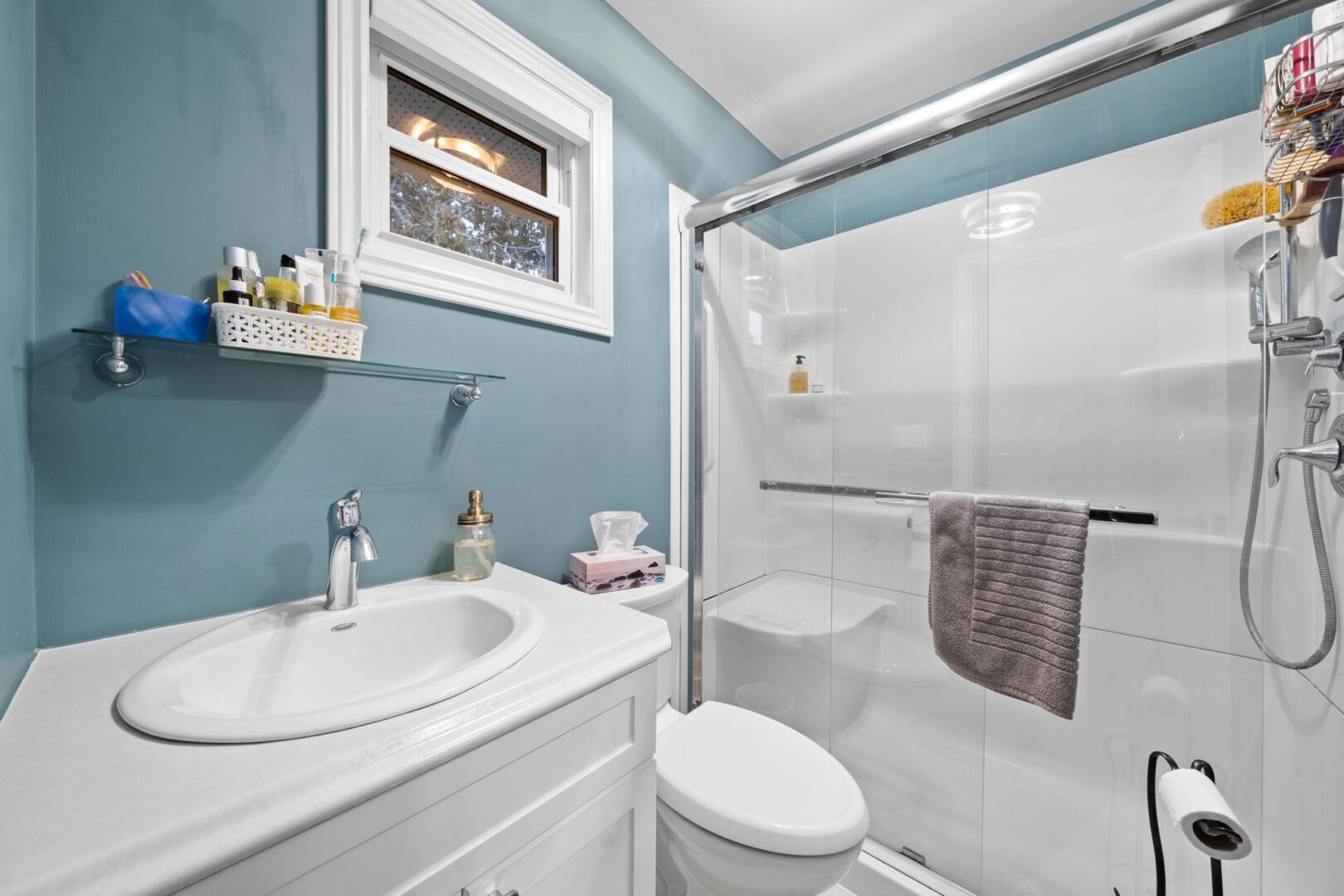 A three-piece bathroom with blue walls, a toilet, a sink, and a walk-in shower.