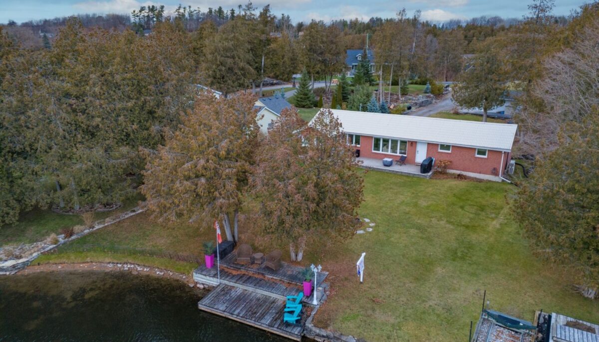 A bungalow on a long lot sits on the shoreline of a river.