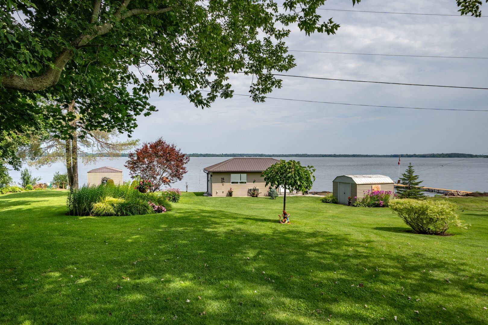 A large, open grassy lot slopes down to the waterfront. A bunkie and a small shed sit near the shoreline.