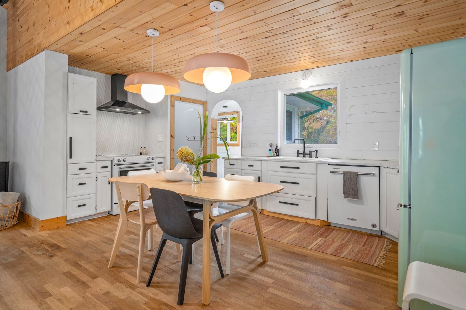 A dining table and chairs sit in the centre of a bright, modern kitchen with white cupboards.