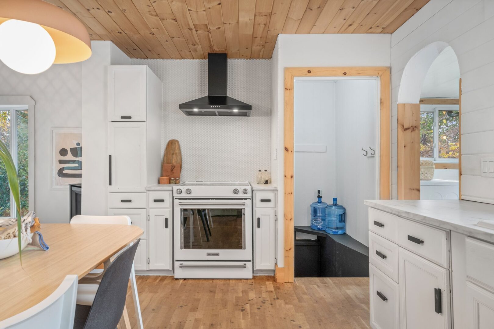 A bright kitchen with hardwood floors and a wood-panelled ceiling. An archway leads into a room off to the right.