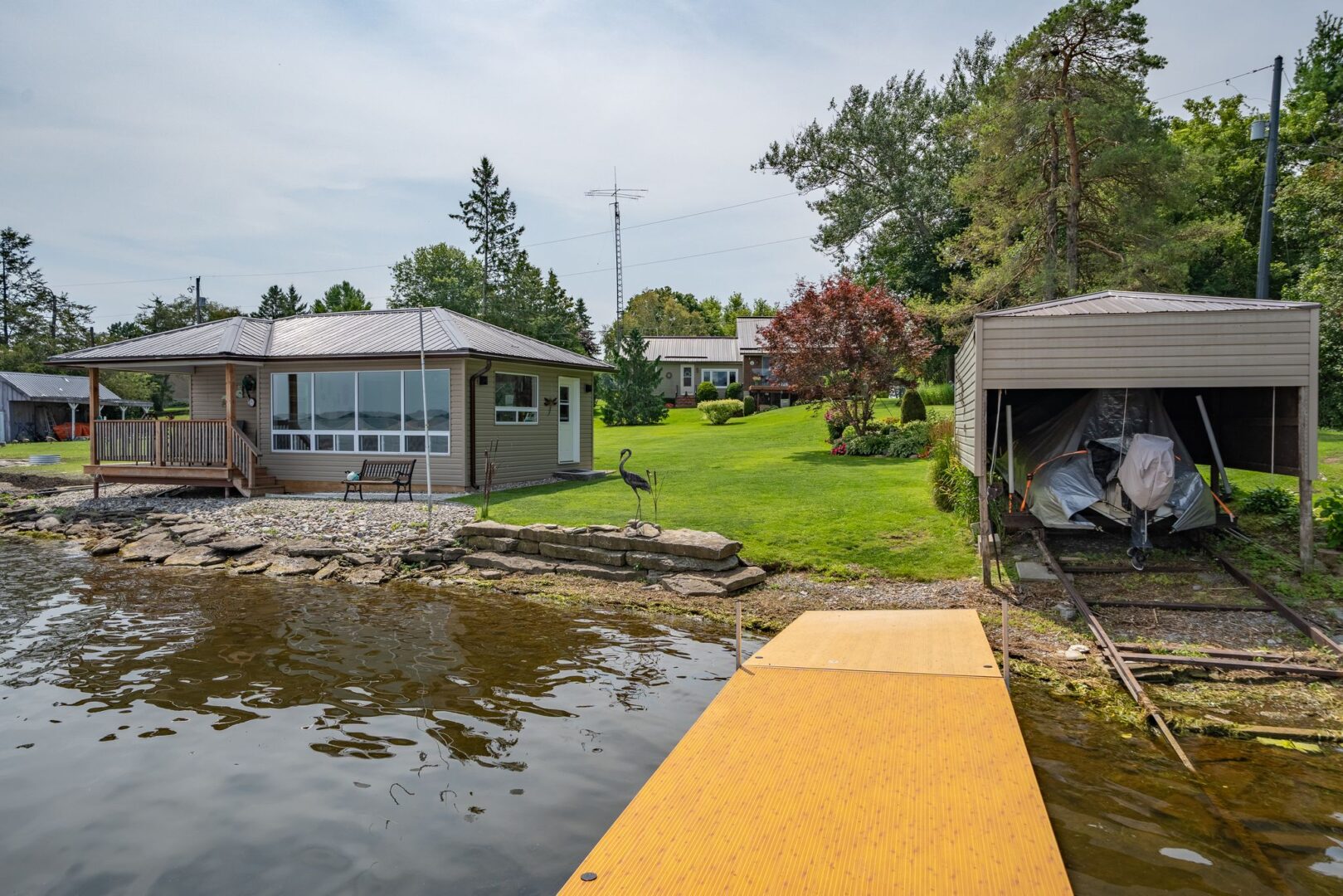 The view up to the shore from a long dock. On the shore sits a bunkie and a small boat launch with a rail system.