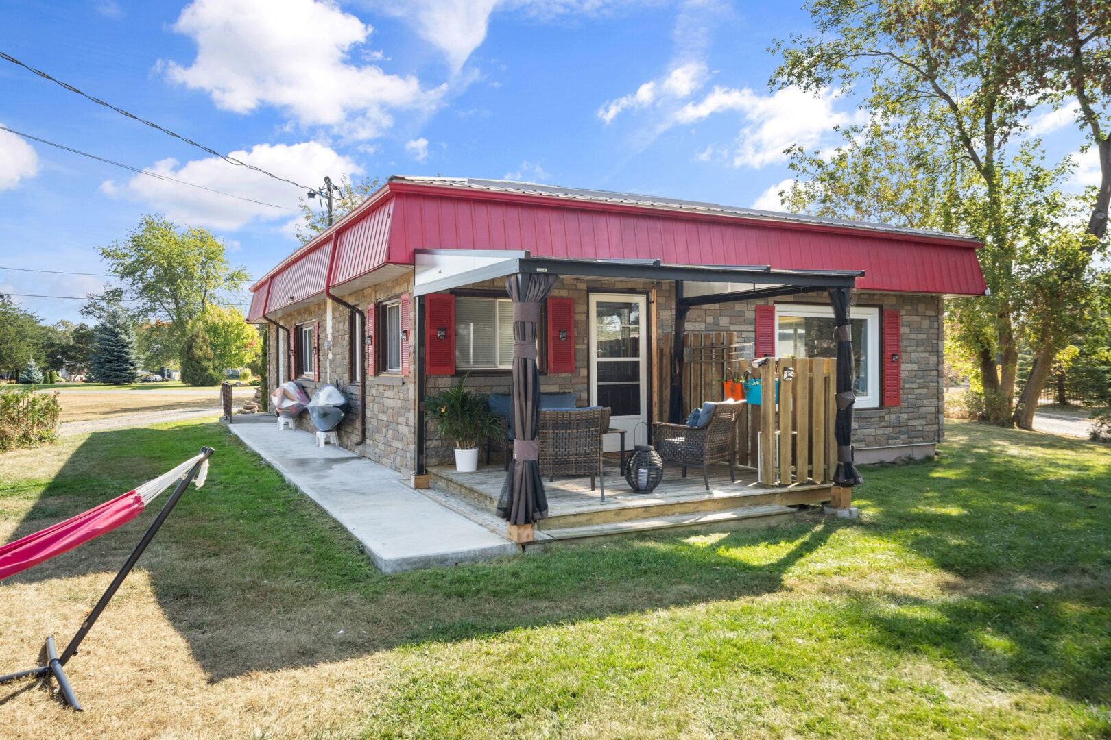 The back of a small bungalow with red roof and window trim. A covered deck with outdoor seating extends off the back of the home.
