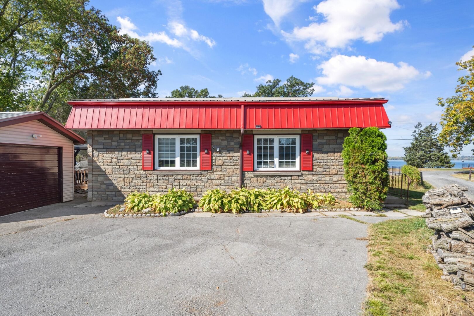 A small bungalow with a red roof, red window trim, and a wide paved driveway.