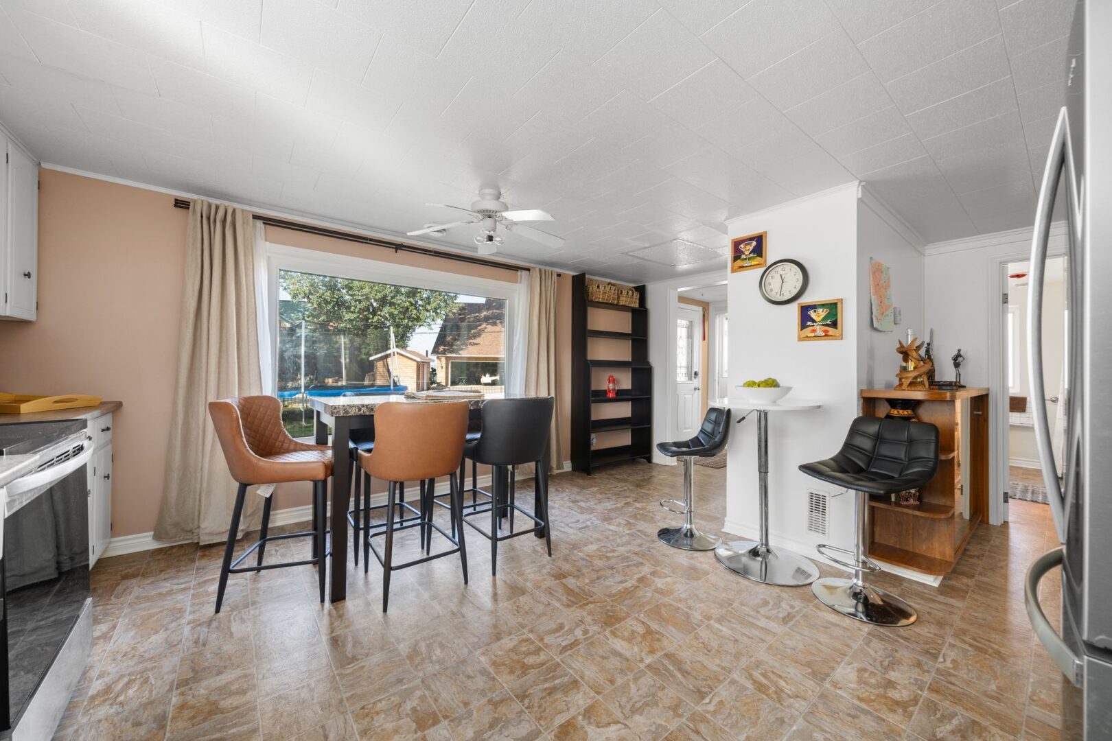 A bright kitchen and dining space with white cupboards, stainless steel appliances, a table and chairs, and a big window.