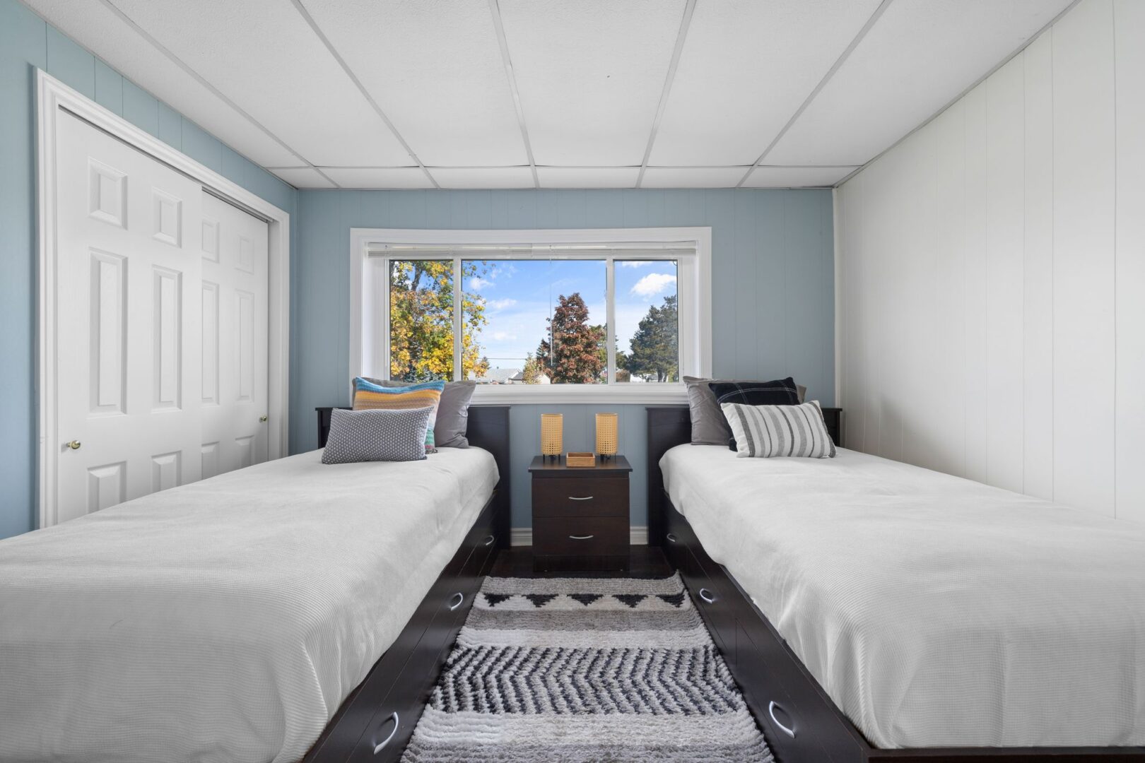 A bright but narrow bedroom with a big window and two single beds.