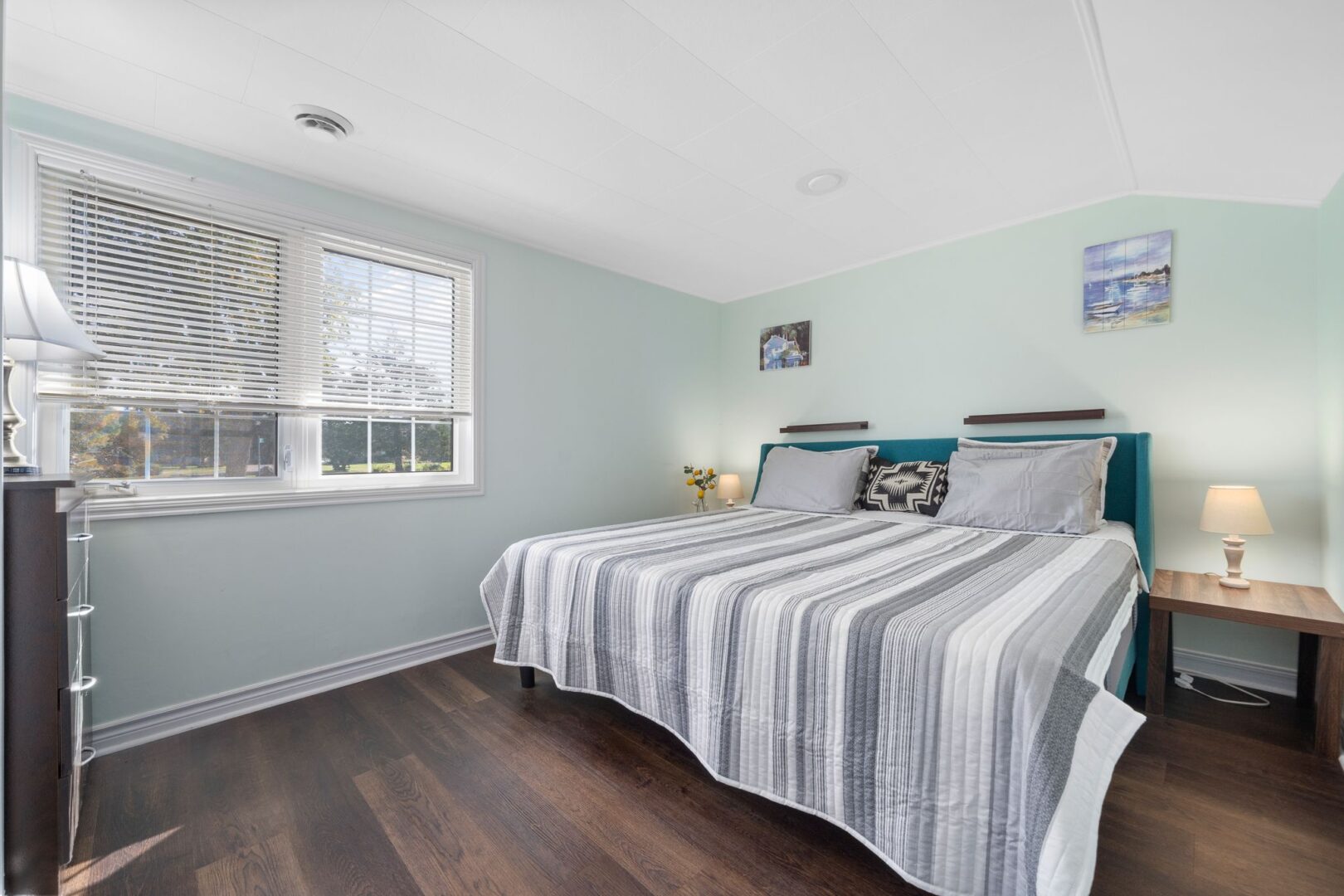 A bright bedroom with a big window, dark wood floors, mint green walls, and a big bed.