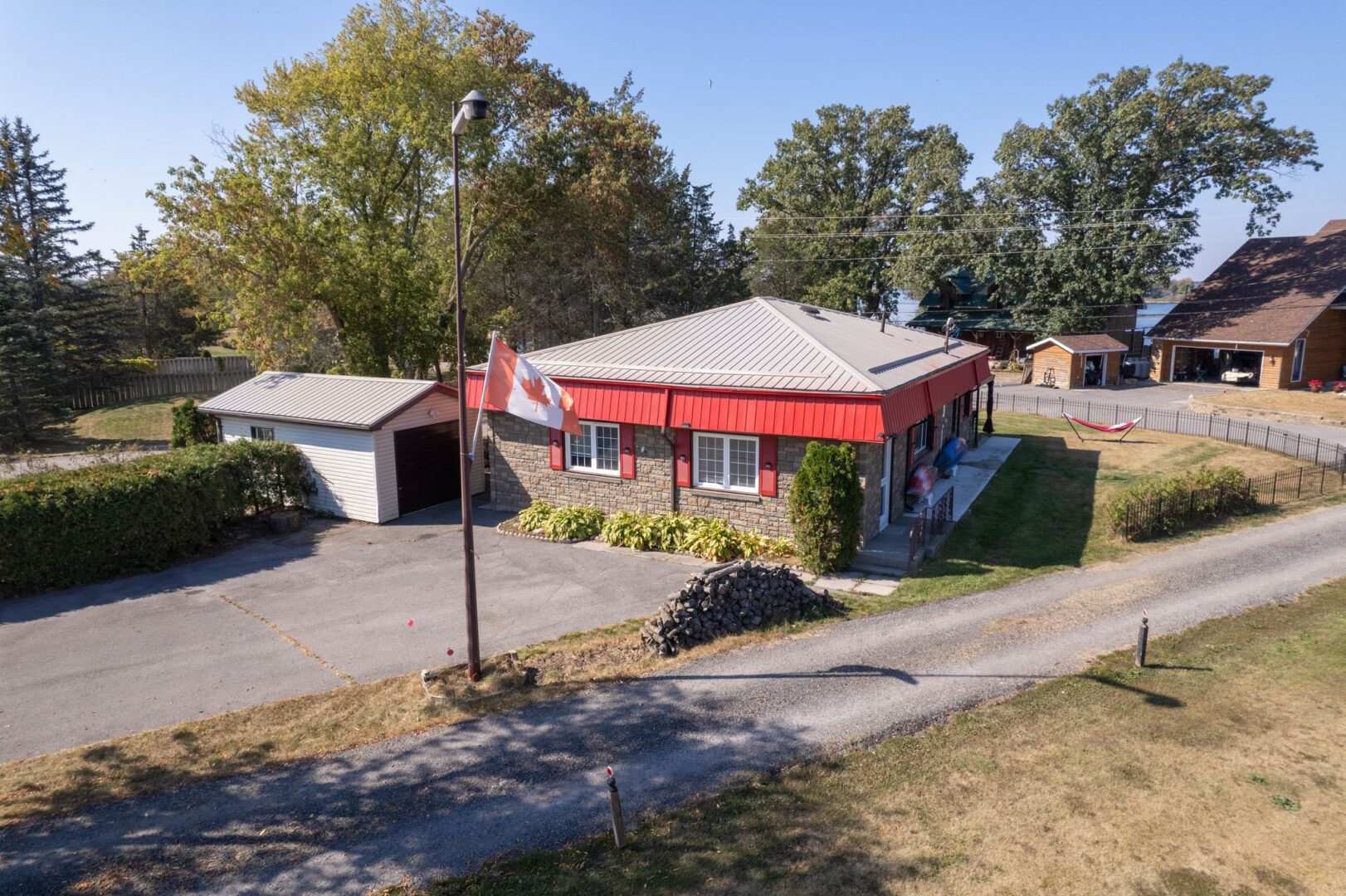 A small bungalow with a red roof, red window trim, a wide paved driveway, and a detached garage.