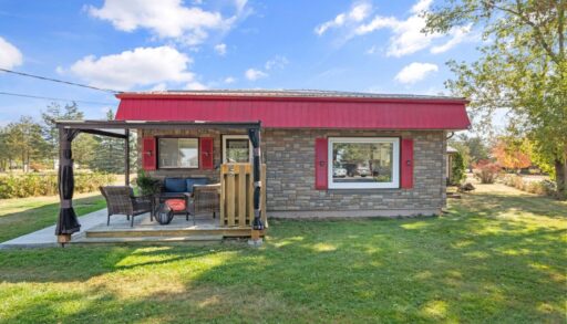 The back of a small bungalow with red roof and window trim. A covered deck with outdoor seating extends off the back of the home.