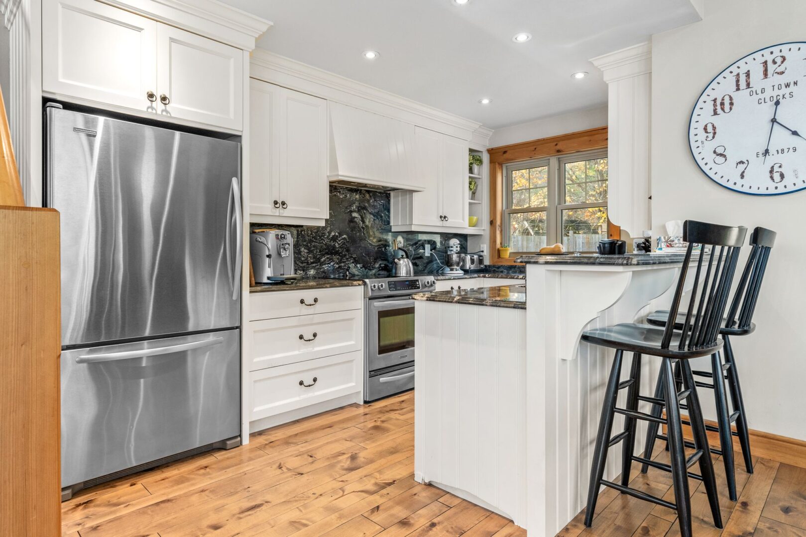 An updated kitchen with hardwood floors, white cupboards, and stainless steel appliances.