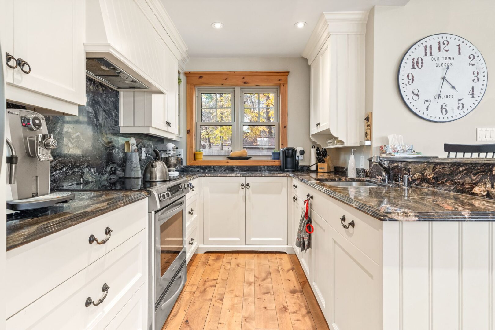 An updated kitchen with hardwood floors, white cupboards, and stainless steel appliances.