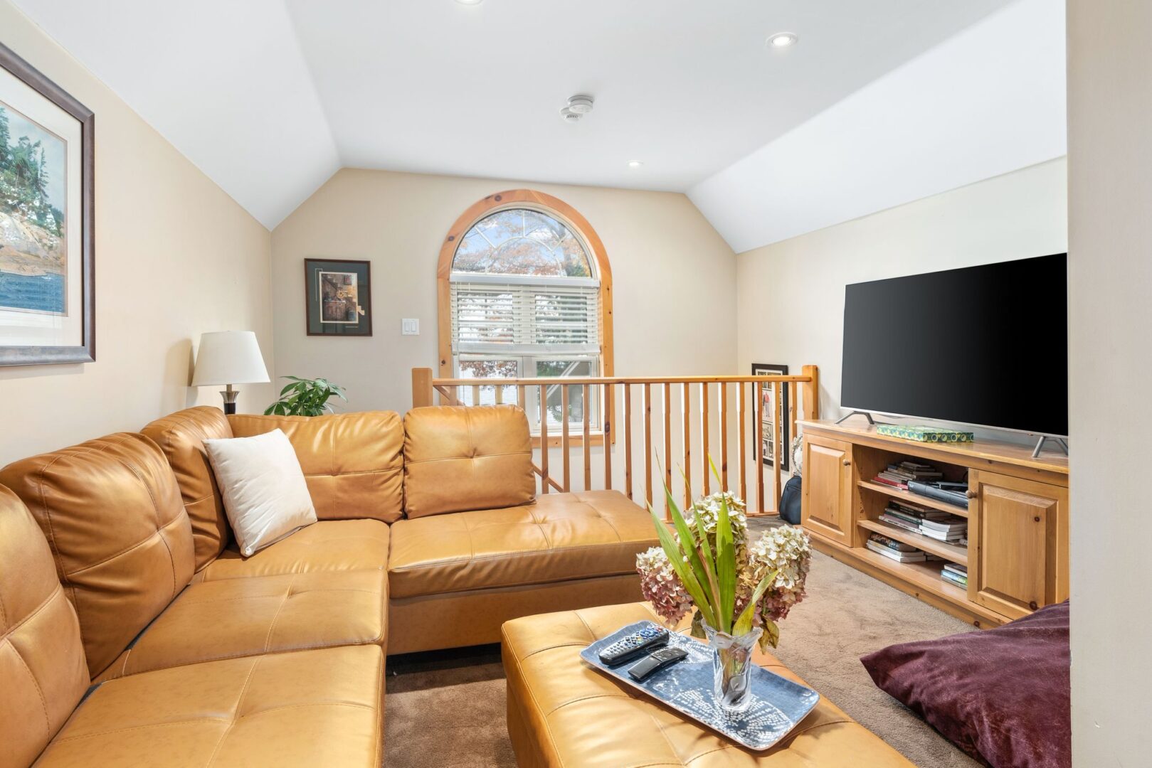 A bright loft living space with a mustard yellow sectional couch and a television.