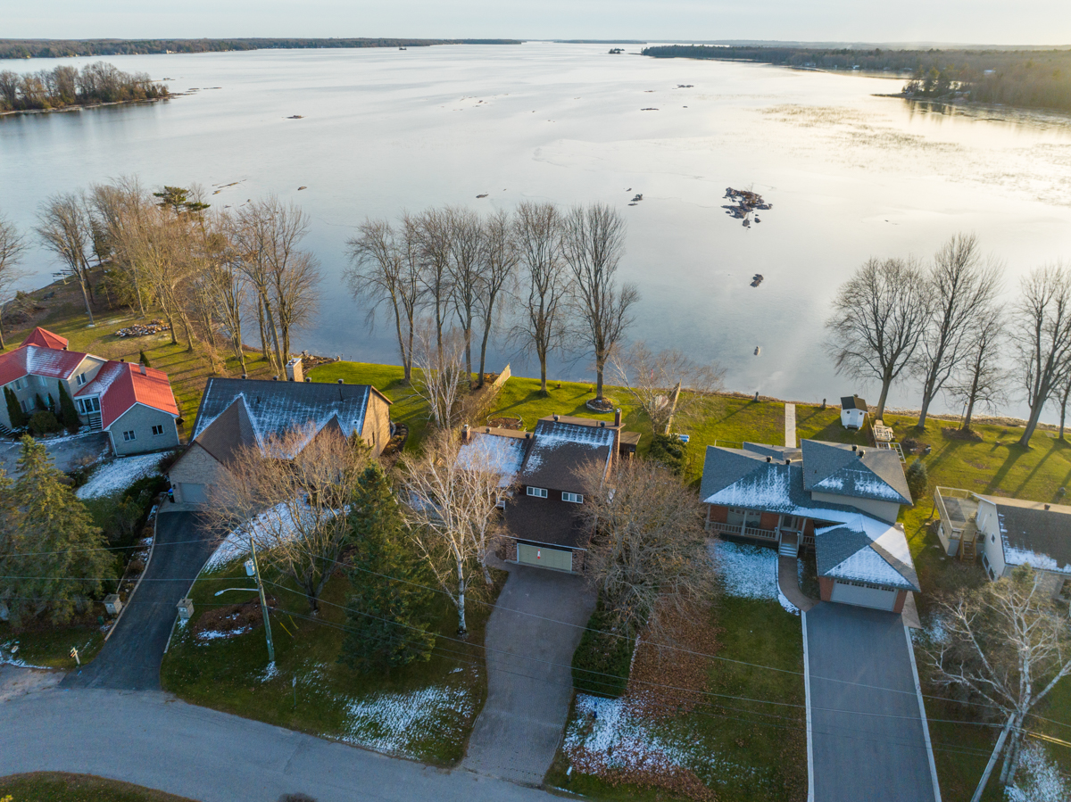 Overhead view of a residential area that backs onto a lake. Waterfront properties line the shore.